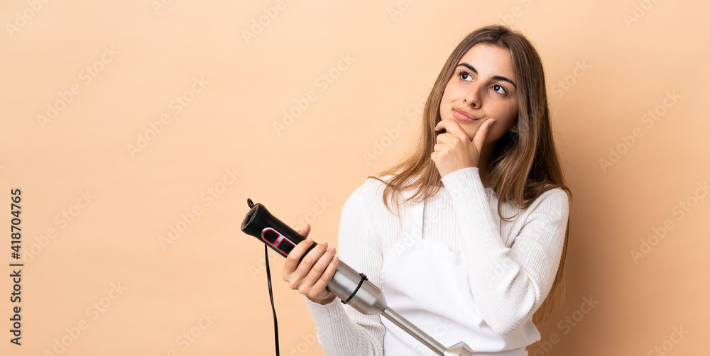 Woman using hand blender over isolated background having doubts Woman using hand blender over isolated background having doubts
