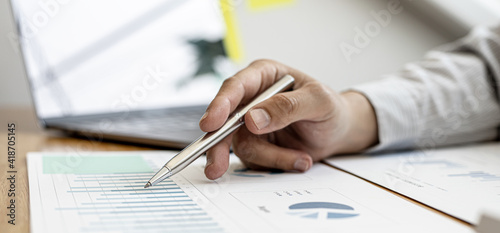 A close-up view of a businessman holding a pen pointing at a bar chart on a company financial document prepared by the Finance Department for a meeting with business partners. Financial concept.