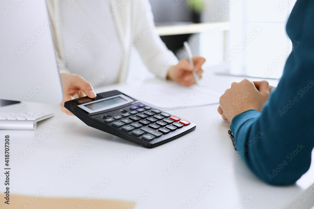 Accountant checking financial statement or counting by calculator income for tax form, hands close-up. Business woman sitting and working with colleague at the desk in office. Audit concept