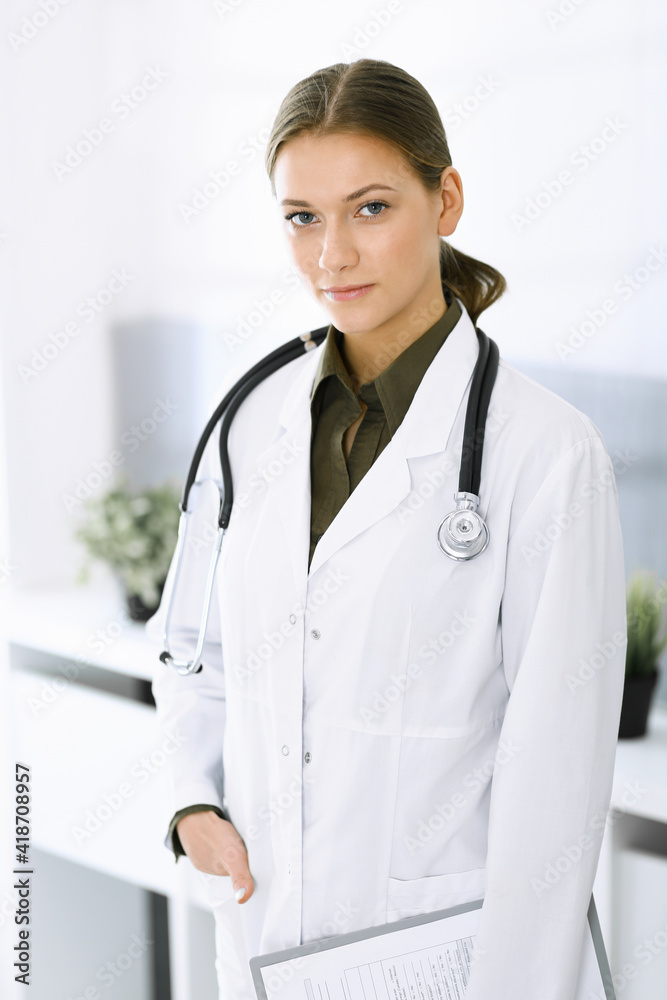 Woman-doctor standing and looking at camera. Perfect medical service in clinic. Medicine and healthcare Woman-doctor standing and looking at camera. Perfect medical service in clinic. Medicine and healthcare