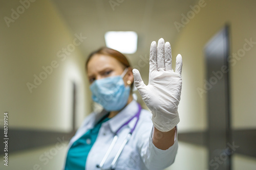 Woman doctor in the hospital corridor. She shows the stop sign with the palm of her hand.