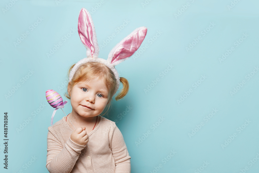 Portrait of a cute little girl dressed in Easter bunny ears holding colorful egg on blue background