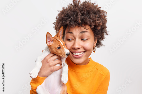 Indoor shot of friendly woman and dog take pleasure while playing together have good relationships enjoy good moment. Positive female pet owner holds small puppy. Animals and people concept. photo