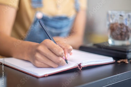 Female hand writing with pen in notebook on counter