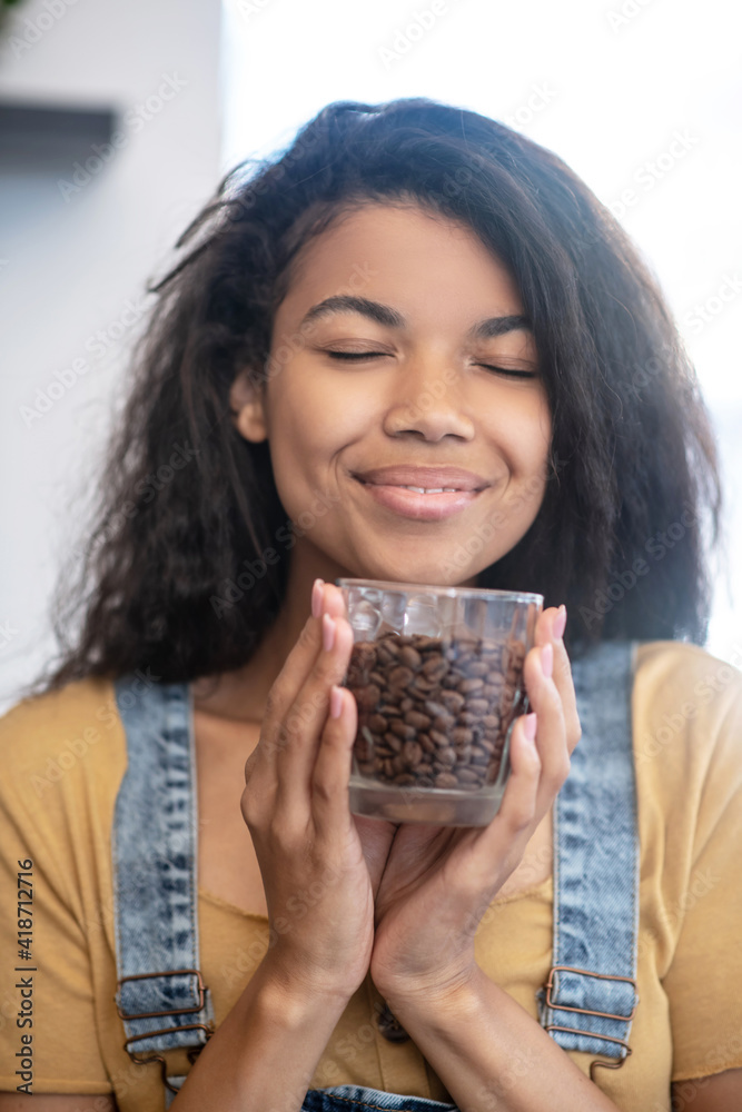 Happy woman with glass of coffee beans near face Happy woman with glass of coffee beans near face