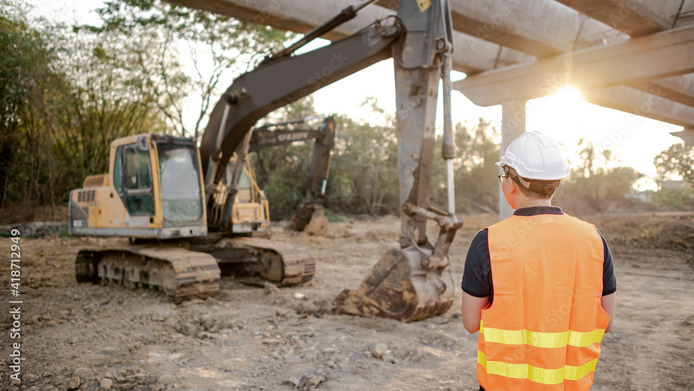 Asian worker man or male civil engineer with protective safety helmet and reflective vest working near excavator machine at construction site. Asian worker man or male civil engineer with protective safety helmet and reflective vest working near excavator machine at construction site.