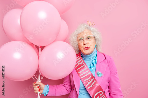 Romantic wrinkled beautiful woman keeps lips folded wants to kiss someone feels thankful for greeting words celebrates her anniversary dressed in festive clothes holds bunch of inflated balloons