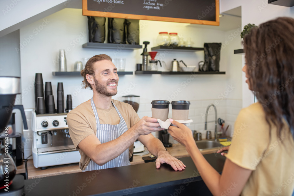 Man at counter giving two coffees to woman Man at counter giving two coffees to woman