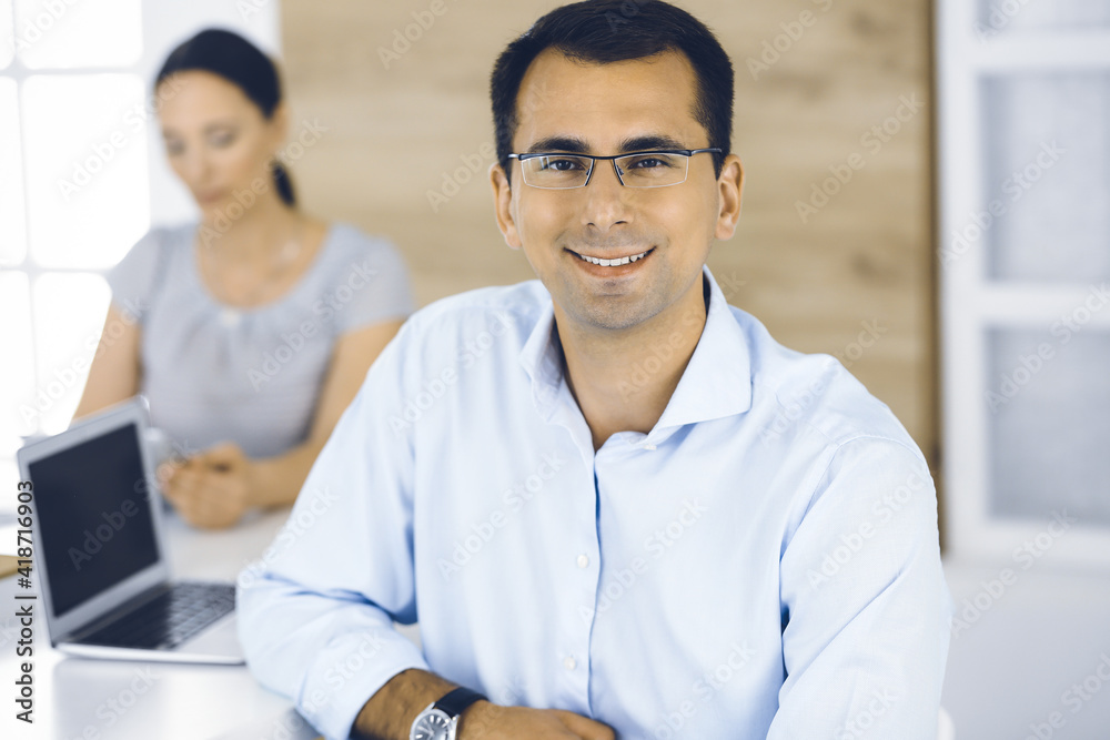 Fototapeta premium Businessman and business woman discussing questions while using a computer in modern office. Portrait of male entrepreneur at meeting. Group of diverse people