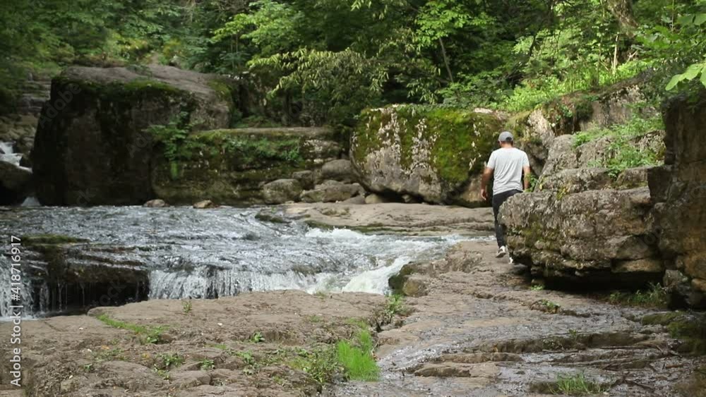 Tourist walks near a forest river with waterfalls. Traveler man Walking Alone near Beautiful Cascade Tropical Waterfall, Enjoying Forest Nature and Relax in Green Jungle. Tourist walks near a forest river with waterfalls. Traveler man Walking Alone near Beautiful Cascade Tropical Waterfall, Enjoying Forest Nature and Relax in Green Jungle.