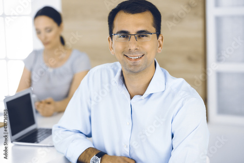Businessman and business woman discussing questions while using a computer in modern office. Portrait of male entrepreneur at meeting. Group of diverse people