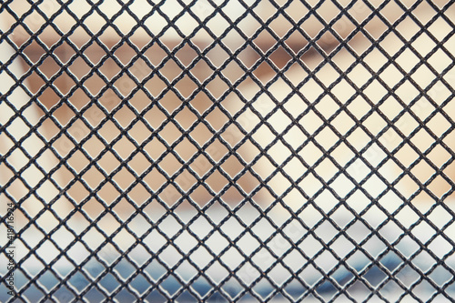 Dark metal fence grid with pattern of numerous small shaped cells installed on light blurred background extreme close view