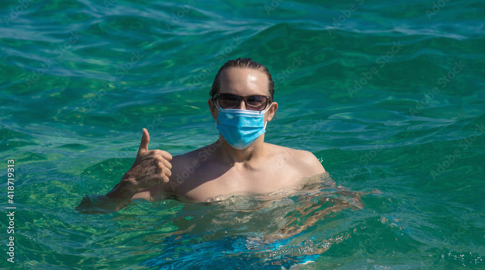 Young man wearing medical mask while swimming in the sea. new normal concept