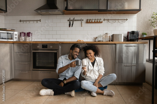 Photography Overjoyed African American couple drinking tea, clinking cups, sitting on kitche