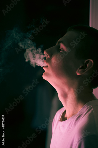 young boy teen smokes, exhales big puffs of smoke
