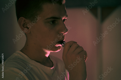 teenager holds a vape in his hand, exhales steam photo