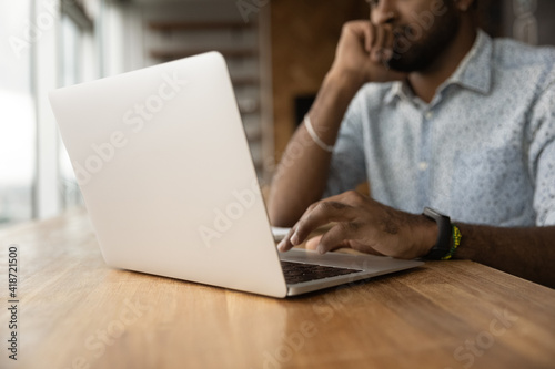 Close up thoughtful African American man using laptop, typing on keyboard, writing message or email, pensive businessman or student working on difficult research project, pondering strategy