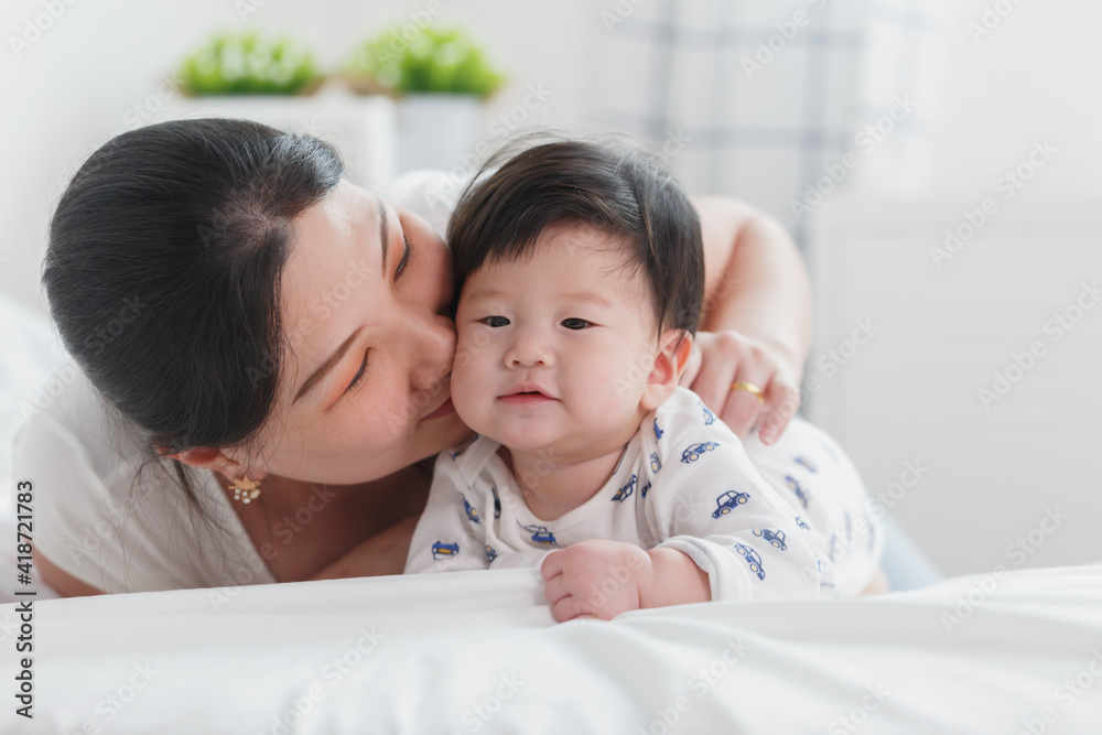 Close up portrait of young beauty Asian mother kissing her newborn baby boy's feet and having fun. Mom playing with her baby. Asia mother's day concept banner Close up portrait of young beauty Asian mother kissing her newborn baby boy's feet and having fun. Mom playing with her baby. Asia mother's day concept banner