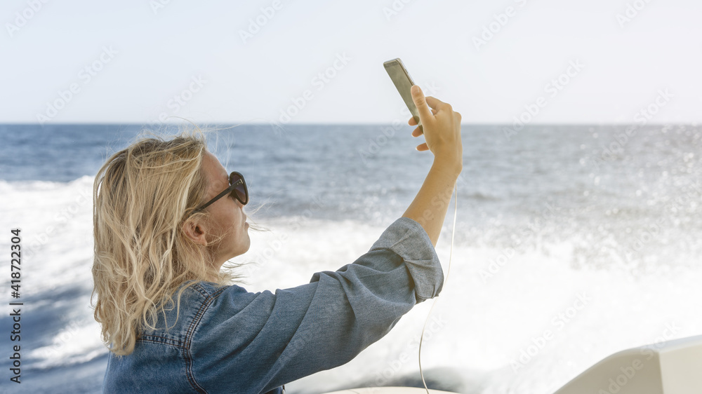 Young woman on luxury yacht taking selfie with phone.