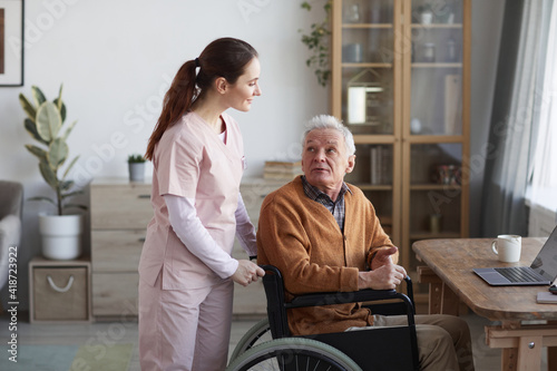 Portrait of senior man in wheelchair looking at caregiver helping him, copy space
