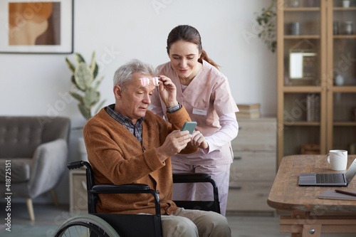 Bild auf Leinwand Portrait of senior man in wheelchair using smartphone with caregiver helping him