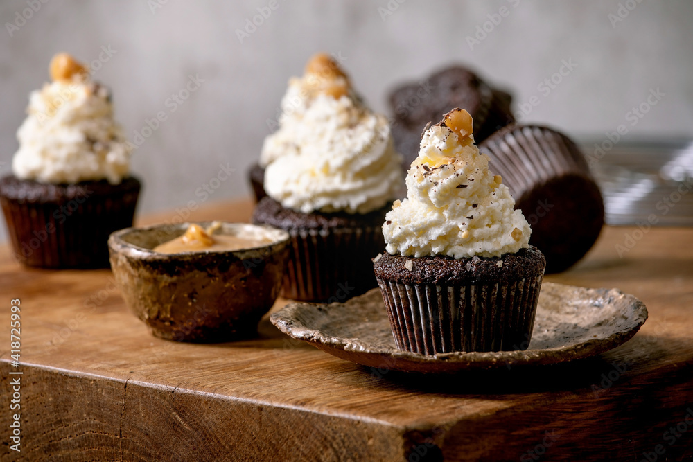 Homemade chocolate cupcakes muffins with white whipped butter cream and salted caramel on ceramic plate on wooden table. Homemade chocolate cupcakes muffins with white whipped butter cream and salted caramel on ceramic plate on wooden table.