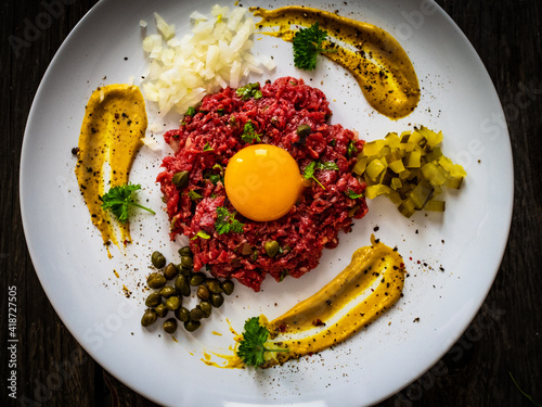 Schilderij op canvas Beef tartare steak with onion, capers and pickled cucumbers on wooden table