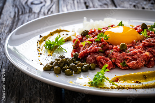 Tablou pe pânză Beef tartare steak with onion, capers and pickled cucumbers on wooden table