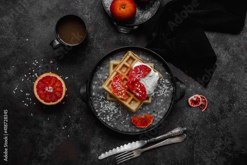 Belgian waffles with a bloody orange on a dark plate. Dark photo