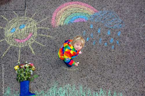 Cute toddler. playing in the rain with chalks, drawing on the asphalt, having fun