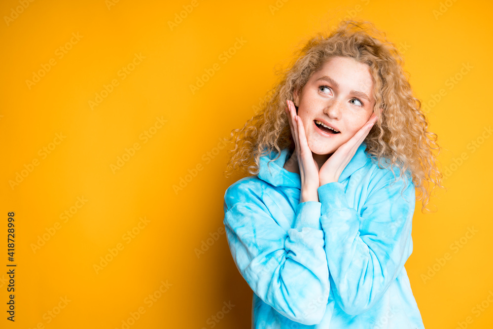 Beautiful smiling woman stands in a blue sweater putting her hands to her face, looking away Beautiful smiling woman stands in a blue sweater putting her hands to her face, looking away