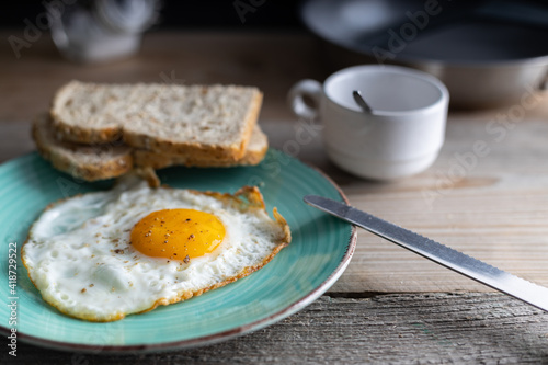 Breakfast fried sunny side up egg with whole grain bread. Fried organic egg sunny side up seasoned with salt and pepper on a plate with whole grain bread on the side. Top view.
