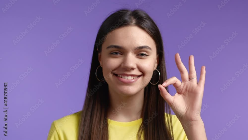 Close-up woman showing Ok sign over violet studio background. Positive young girl smiles to camera. Winner. Success. Body language. Close-up woman showing Ok sign over violet studio background. Positive young girl smiles to camera. Winner. Success. Body language.