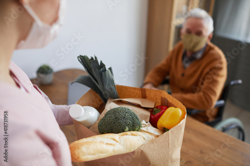 Close up of young woman bringing groceries to senior man in wheelchair, food delivery service concept, copy space