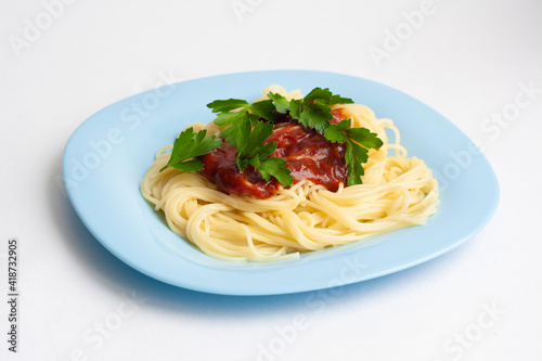 Spaghetti pasta with tomato sauce and herbs in a blue plate on a white background
