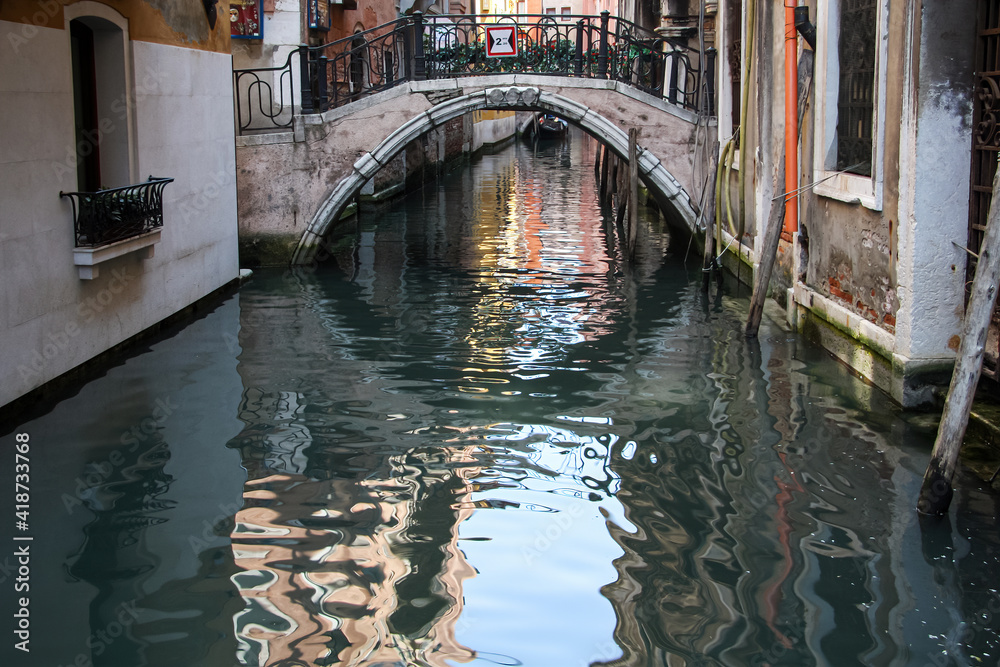 Canals of Venice on a bright summer day. Typical canal of Venice, with the reflection of houses and the sky in the water, an old bridge with wrought iron railings.