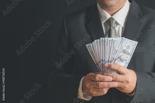 business man wearing suit and necktie holding money in hand on black background, US dollar (USD) bills