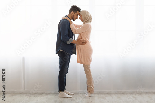 Romantic muslim spouses expecting baby standing together against window at home