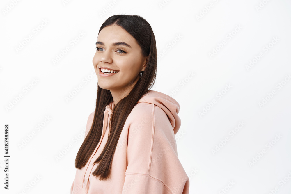Profile shot of smiling young woman looking happy at left side copy space, wearing pink hoodie, standing against white background Profile shot of smiling young woman looking happy at left side copy space, wearing pink hoodie, standing against white background
