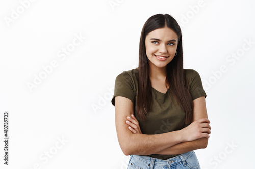 Beautiful young healthy woman smiling, looking away at logo copy space, standing with arms crossed on chest against white background, wearing casual t-shirt