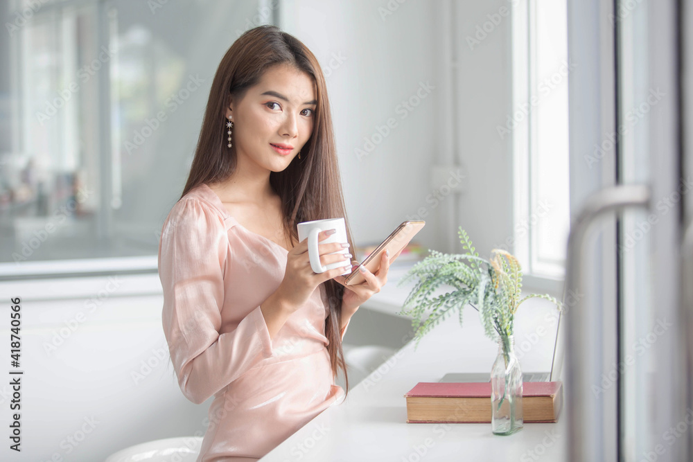 A beautiful girl working in the office With a computer, a phone and a mug of coffee happily A beautiful girl working in the office With a computer, a phone and a mug of coffee happily