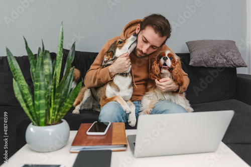 Canvas Print Man hugging with dogs while working at laptop while sitting on sofa at home