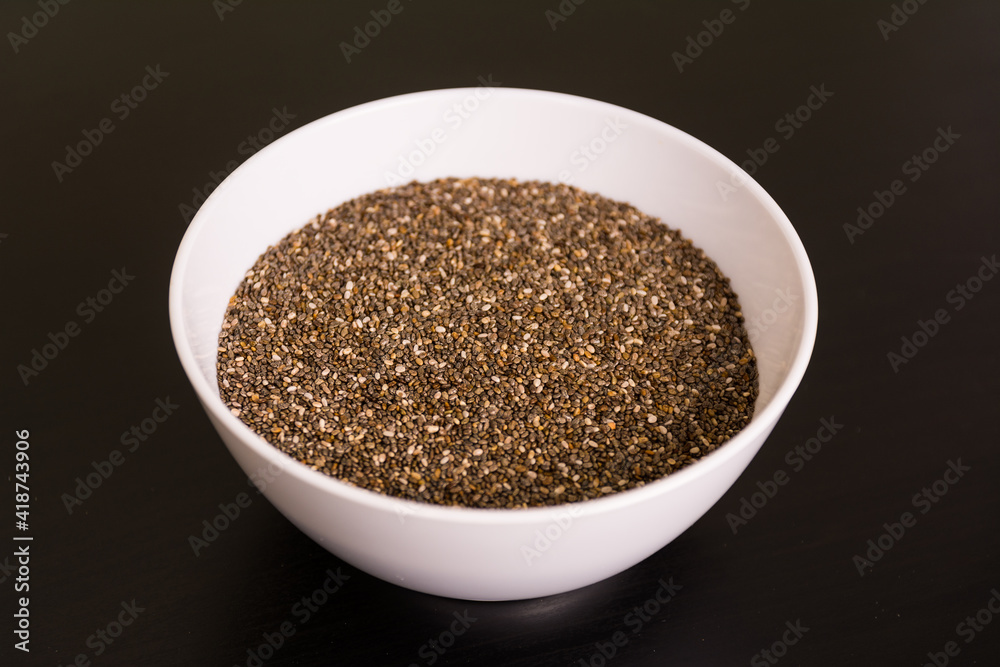 pile of chia seeds in round white bowl on black table top view pile of chia seeds in round white bowl on black table top view