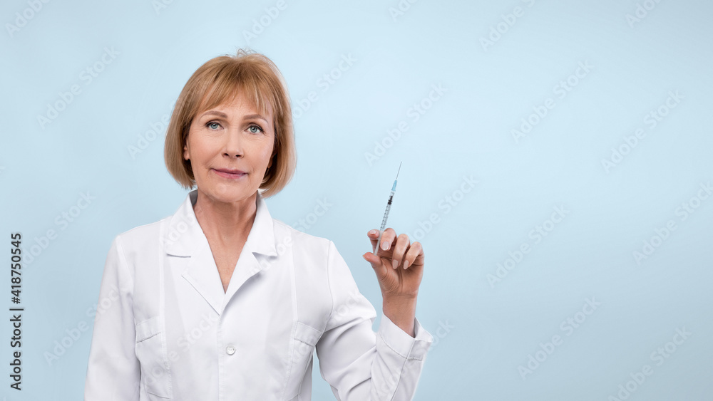 Senior female doctor with syringe looking at cmera on blue studio background, banner design with empty space Senior female doctor with syringe looking at cmera on blue studio background, banner design with empty space