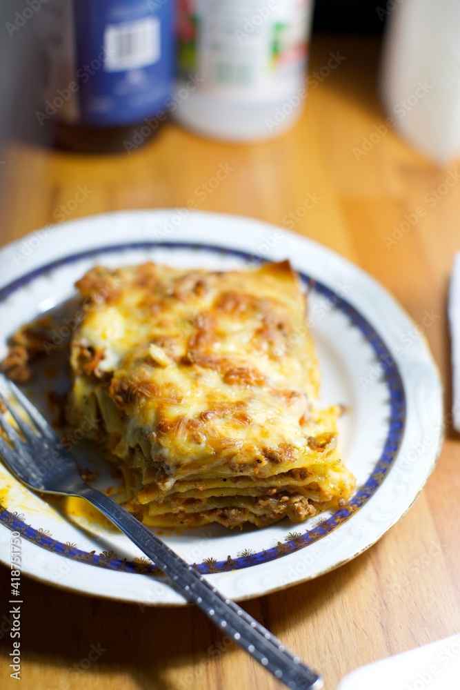 home made lasagna in a white plate and on the wooden desk. blurry background.