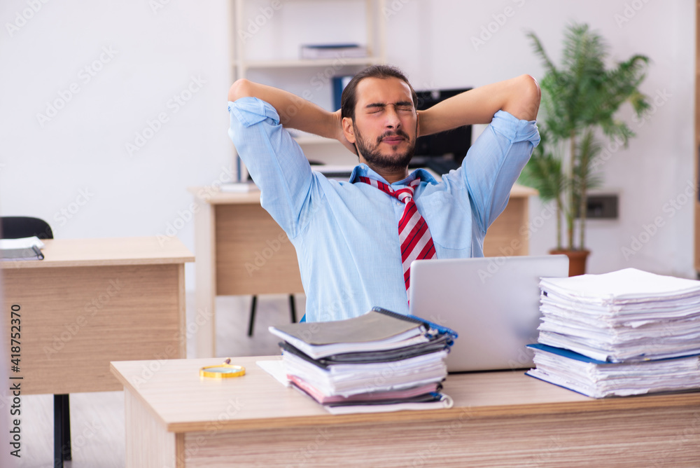 Young male employee unhappy with excessive work in the office Young male employee unhappy with excessive work in the office