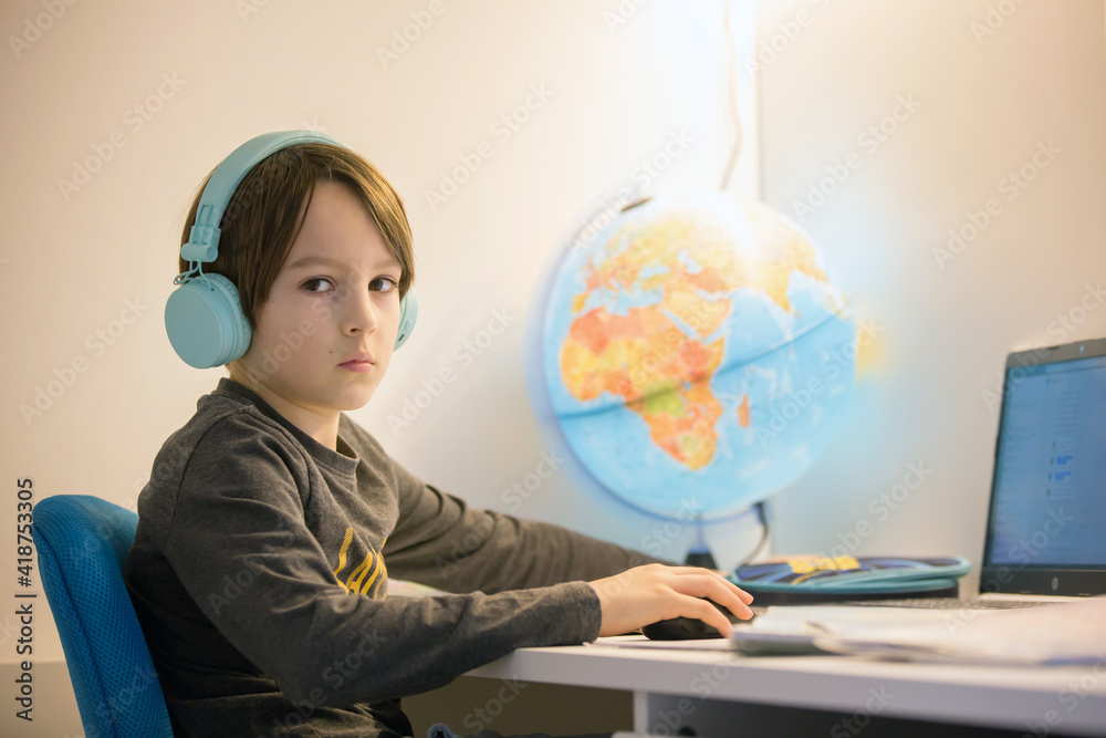 Beautiful child with earphones using laptop while studying at desk at home Beautiful child with earphones using laptop while studying at desk at home