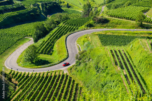 Beautiful vineyard landscape showing a red car driving up a curvy mountain pass road at the Kaiserstuhl, Germany. 