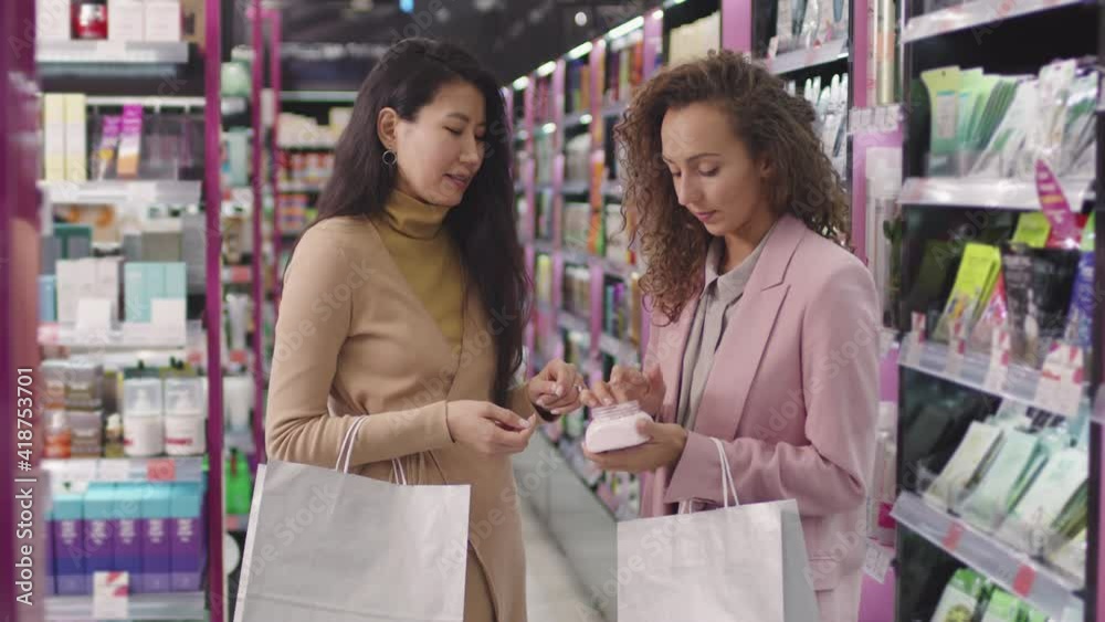 Slow-motion medium shot of attractive multi-ethnic women standing in cosmetics store shopping, testing different skin care products Slow-motion medium shot of attractive multi-ethnic women standing in cosmetics store shopping, testing different skin care products