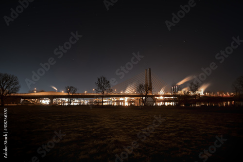 Ein Industriepark am Fluss mit einer Brücke - nachts beleuchtet mit Spieglungen im Wasser